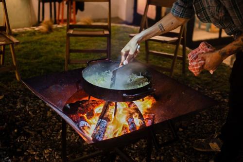 a person cooking food in a pan on a grill at Hostel Hormiga Negra in San Carlos de Bariloche