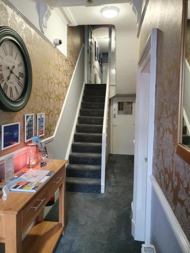 a hallway with a staircase with a clock on the wall at The Braemar Southport in Southport