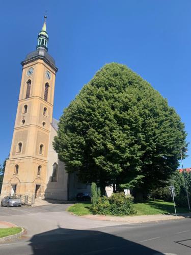 uma grande árvore em frente a uma igreja com uma torre de relógio em Apartmán na horách em Vejprty