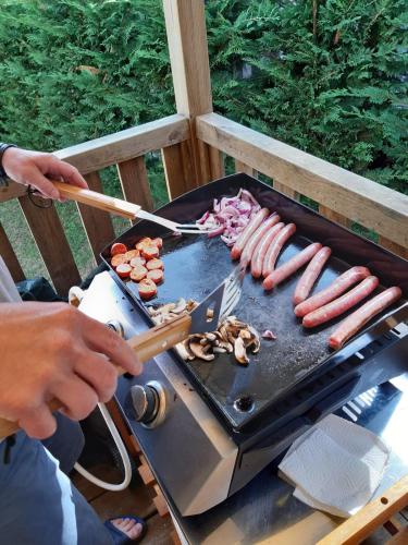 a person cooking sausages and onions on a grill at Les Charmettes - SIBLU in Les Mathes