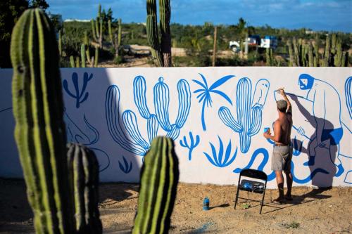 a man painting a mural on a wall with cactus at La Ventana Hostel in La Ventana