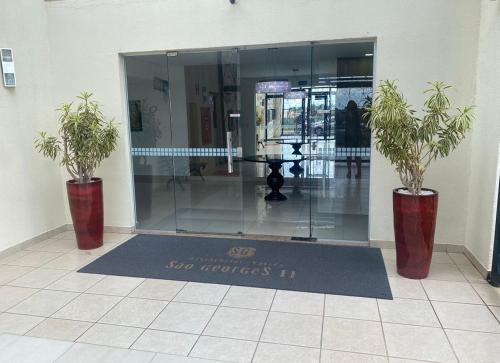 a lobby with two potted plants in front of a glass door at Apto 3 Quartos com Ar, Piscina, Garagem - Cuiabá in Cuiabá