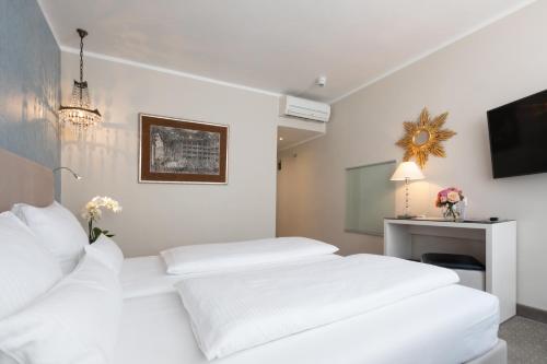 a white bedroom with two white beds and a television at Hotel an der Oper in Munich