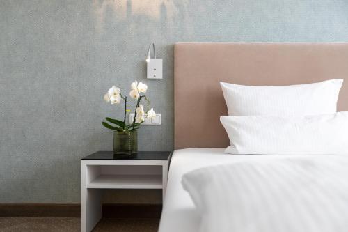 a bed with a table with a vase of flowers on it at Hotel an der Oper in Munich