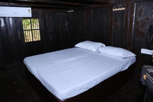 a bed with white sheets and pillows in a wooden room at Aqualillies Water Front Heritage Homestay in Kumarakom
