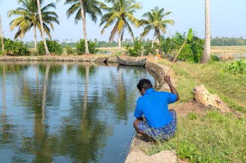 a person sitting on the side of a river with a pole at Aqualillies Water Front Heritage Homestay in Kumarakom