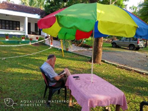 a man sitting at a table under an umbrella at Aqualillies Water Front Heritage Homestay in Kumarakom