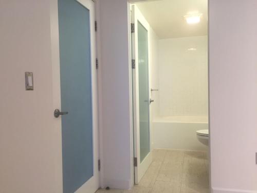 a white bathroom with a toilet and a doorway at Huge Downtown LA Loft with Rooftop Pool & Jacuzzi in Los Angeles