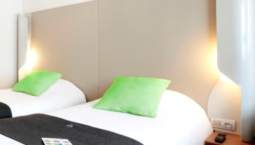 a bedroom with two white beds with green pillows at Campanile Valenciennes - Petite-Forêt in Petite Forêt