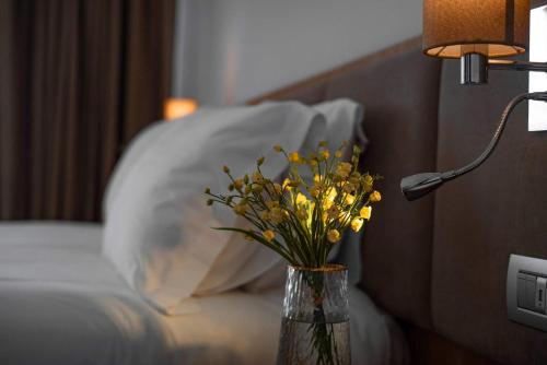 a vase of yellow flowers on a table next to a bed at Amare Hotel in Shëngjin