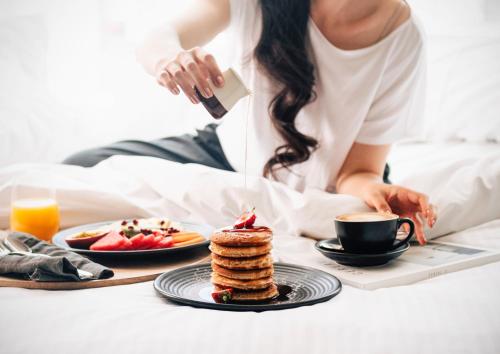 a woman in bed with a plate of pancakes and a cup of coffee at Novotel Chennai OMR in Chennai