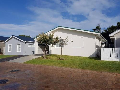 a white house with a tree in the front yard at Pearly Waves in Pearly Beach