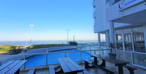 a building with a swimming pool with benches and the ocean at Tranquil Impulse on Strand in Cape Town