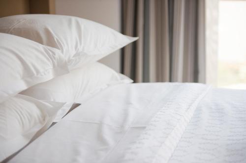 a white bed with white pillows and a window at Premier Hotel Quatermain in Johannesburg
