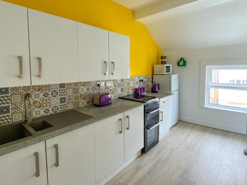 a kitchen with white cabinets and a yellow wall at 'Llandudno Central' - 2 Bed Luxury Flat, Close to Town and Beaches in Llandudno
