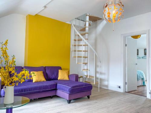 a purple couch in a living room with a yellow wall at 'Llandudno Central' - 2 Bed Luxury Flat, Close to Town and Beaches in Llandudno
