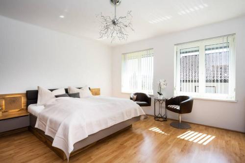 ein weißes Schlafzimmer mit einem großen Bett und zwei Fenstern in der Unterkunft Schönes Ferienhaus mit Garten in Pörtschach am Wörthersee