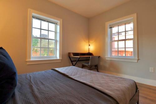 a bedroom with a bed and a desk and two windows at The Old Town Suite at Prince Street Inn in Alexandria