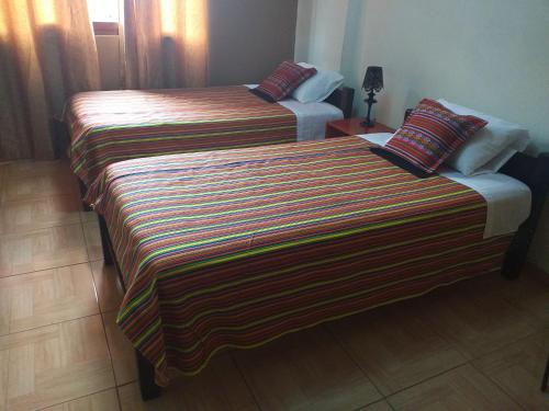 two beds in a hotel room with a striped blanket at Chakana Family Home Lima Airport in Lima