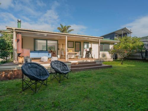 a house with two chairs in front of a yard at Idyll Thyme - Hahei Holiday Home in Hahei