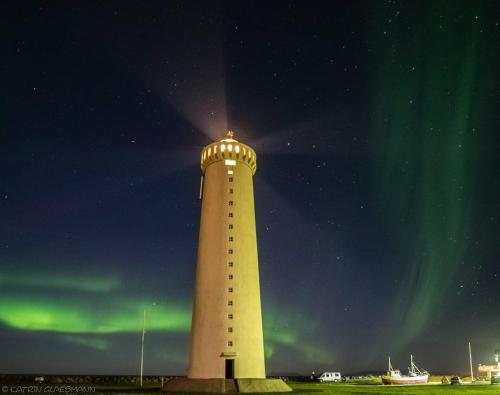 a lighthouse with the aurora in the sky behind it at Garður Apartments in Gardur