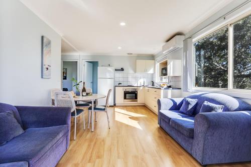 a living room with two blue couches and a kitchen at Beach Cabins Merimbula in Merimbula