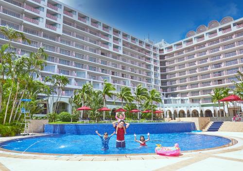 a family standing in a swimming pool in front of a hotel at Hotel Mahaina Wellness Resorts Okinawa in Motobu
