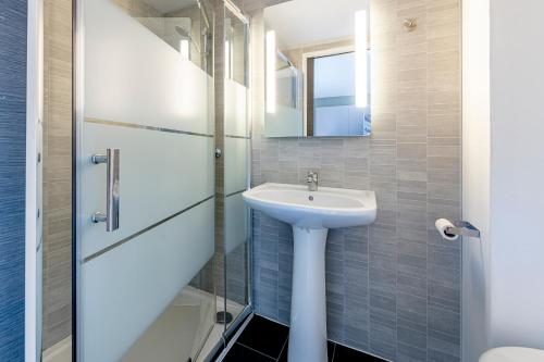 baño con lavabo y puerta de ducha acristalada en B&B HOTEL Bordeaux Le Haillan, en Le Haillan
