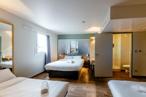 a hotel room with two beds and a bathroom at B&B HOTEL Bordeaux Le Haillan 3 étoiles in Le Haillan