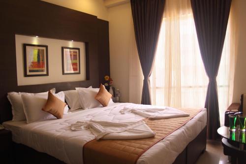 a bedroom with a bed with white sheets and a window at Hotel Pristine Residency in Ahmedabad