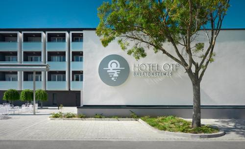 un árbol delante de un edificio con un cartel en Hotel OTP Balatonszemes, en Balatonszemes