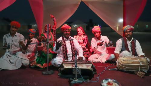 um grupo de pessoas sentadas em um palco em Shiv Tara Desert Camp em Sām