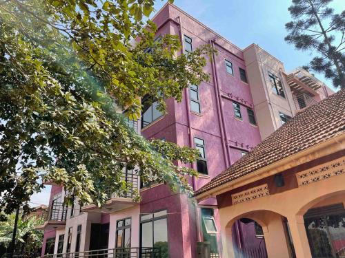 a pink building in front of two houses at Jaffa Suites in Kampala