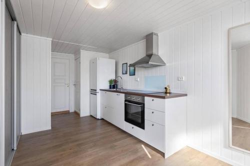 La cuisine est équipée de placards blancs et d'un four avec plaques de cuisson. dans l'établissement Apartment with amazing views - free parking, à Arendal