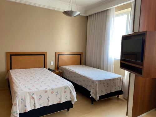 a hotel room with two beds and a flat screen tv at Flat, Savassi Condomínio Century in Belo Horizonte