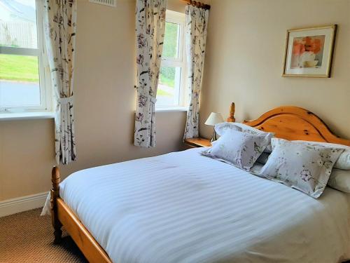a bedroom with a large white bed with two windows at Abhainn Ri Cottages in Blessington