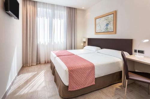 a hotel room with a bed, desk, chair and lamp at Catalonia Hispalis in Seville