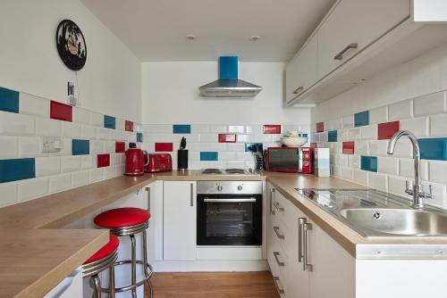 a kitchen with white cabinets and red and blue tiles at Violets Wonderland Cottage in Llandudno