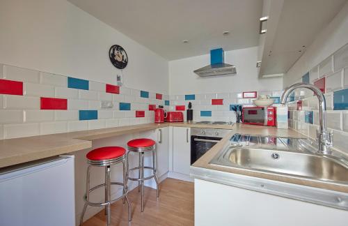 a kitchen with a sink and two red stools at Violets Wonderland Cottage in Llandudno