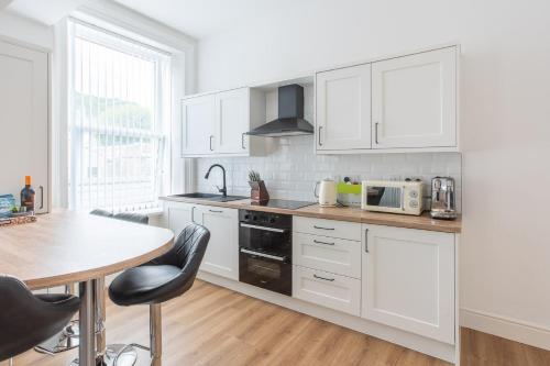 cocina con armarios blancos y mesa de madera en Banc Apartment 1 en Porthmadog
