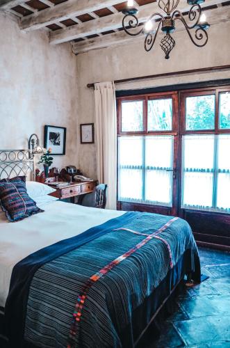a bedroom with a bed and a desk and windows at Meson Panza Verde in Antigua Guatemala