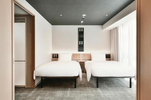 two beds in a room with a table and chairs at REF Matsuyama City Station by VESSEL HOTELS in Matsuyama