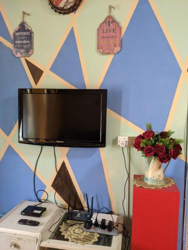 a television on a wall above a stove with a vase of flowers at Salam D'Mawar Homestay in Sungai Coh
