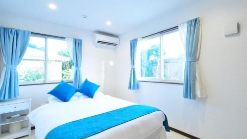 biała sypialnia z niebieskimi zasłonami i łóżkiem w obiekcie Sunshoen Akaishibeach w mieście Hirakubo