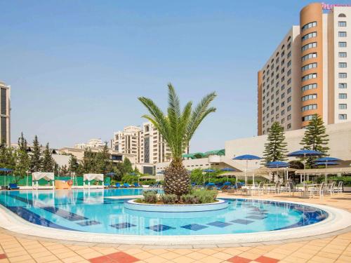 a swimming pool with a palm tree in a resort at Hotel Mercure Alger Aéroport in Dar el Beïda