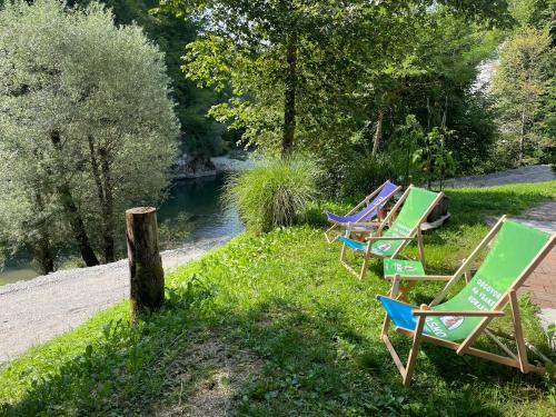 four lawn chairs sitting in the grass next to a river at Okrepčevalnica Kurn'k in Cerkno