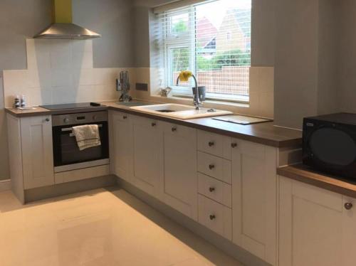 a kitchen with white cabinets and a sink and a window at Inviting 2-Bed Bungalow in Heacham with spa bath in Heacham