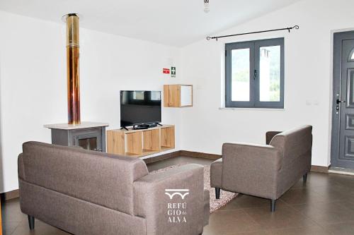 a living room with two chairs and a couch and a television at Refúgio do Alva - Serra da Estrela in Seia
