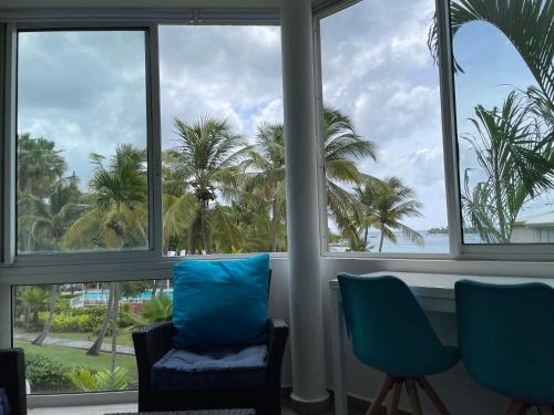 a room with windows with blue chairs and palm trees at Résidence de la Vieille Tour in Le Gosier