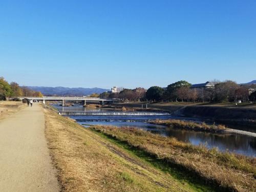 a path next to a river with a bridge in the background at Kasuian in Kyoto